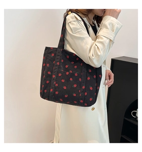 Detailed texture of black corduroy tote bag with red strawberry pattern on a shoulder strap