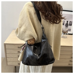 Detail of black large hobo bag featuring a cute brown bear charm and a striped ribbon