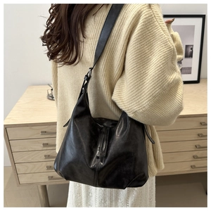 Detail of black leather hobo bag featuring a vertical strap buckle and wide shoulder strap