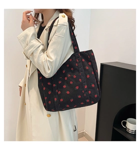 Close-up of black corduroy strawberry tote bag with front pocket shown on a model