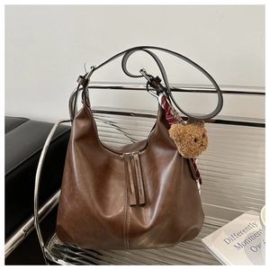 Detail of vintage brown PU leather hobo bag with teddy charm and plaid scarf on a chair