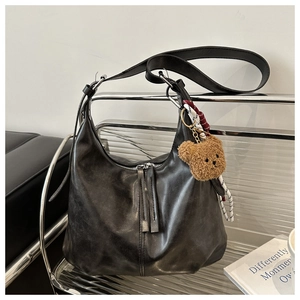 Detail of black leather hobo bag with teddy bear charm and woven strap accents