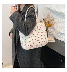 Detail of white corduroy tote bag with strawberry prints worn over a grey wool coat