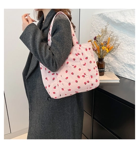 Detail of pink corduroy tote bag with red strawberry print and front pocket on shoulder