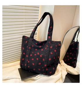 Close-up of black corduroy tote bag featuring red strawberry print and front pocket