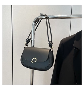 Detail of minimalist black saddle bag featuring gold metal buckle and knotted strap