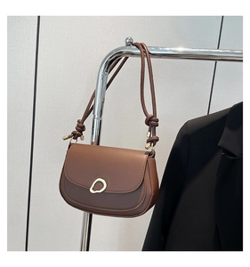 Detail of a brown saddle bag with a golden oval metal buckle and thin knotted shoulder strap