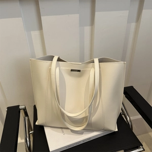 Chic cream leather tote bag with long shoulder straps on a modern black chair