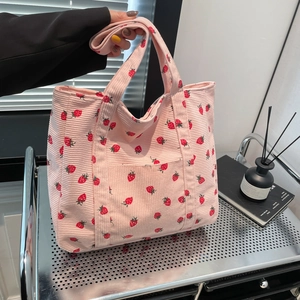 Pink corduroy tote bag with strawberry print and shoulder strap shown in lifestyle setting