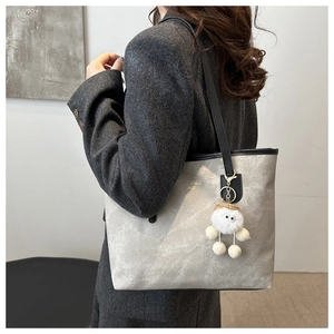 Dettaglio della borsa tote grigia con ciondolo di peluche e tracolla su modella