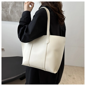 Side view of a white PU leather tote bag worn by a model in a modern interior setting