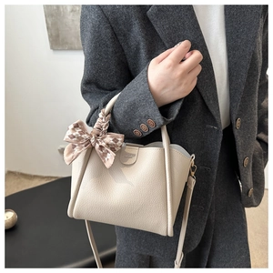 Creamy off-white leather bucket bag detail with a brown plaid bow and handle