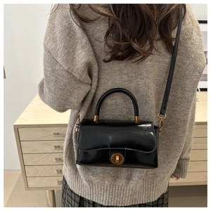 Modèle portant un sac bandoulière noir brillant avec fermoir rond et sangle réglable