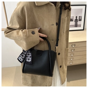 Détail du sac seau noir en cuir grainé avec un foulard décoratif en soie à carreaux chic