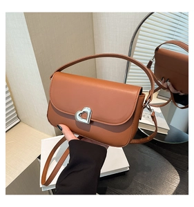 Detail of a brown leather saddle bag featuring a silver heart-shaped metal twist lock closure