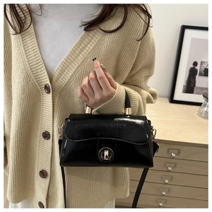 Detail of glossy black leather crossbody bag featuring a golden circular twist lock