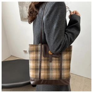Lifestyle view of large plaid tote bag worn on shoulder over grey coat in a soft setting