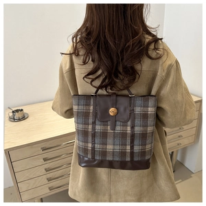 Detail of plaid tote bag with brown leather flap and engraved metal N-button closure
