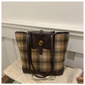 Detail showing the brown plaid fabric texture and leather strap with a gold metal button