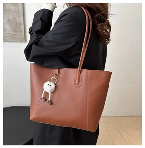 Detail of vintage brown tote bag with cute white plush monster charm on shoulder