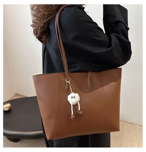 Detail of minimalist dark brown leather tote bag with creative long-legged plush charm