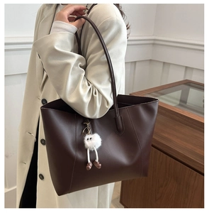 Detail of dark brown tote bag with fuzzy monster charm shown on model's shoulder
