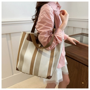 Detail of striped canvas tote bag with brown leather handles and protective corners