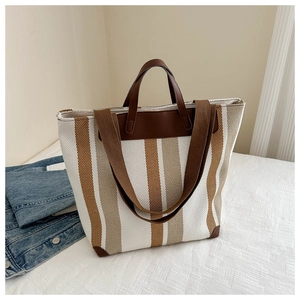 Close-up of striped canvas tote bag with leather handles and reinforced corner detail