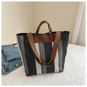 Close-up of black and white striped canvas tote with brown leather handle reinforcement