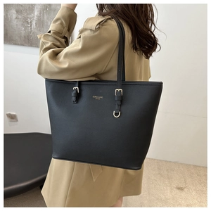Detail of minimalist black leather tote bag with gold lettering shown on model's shoulder