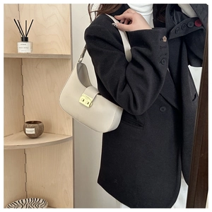 Detail of a creamy white half-moon shoulder bag with a gold buckle worn on a shoulder