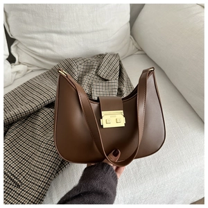 Detail of dark brown crescent bag with gold clasp closure on white fabric sofa
