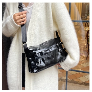 Detail of black glossy PU leather shoulder bag with metallic buckle straps on a model