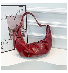 Detail of burgundy glossy leather handbag with pleated side and decorative strap knot