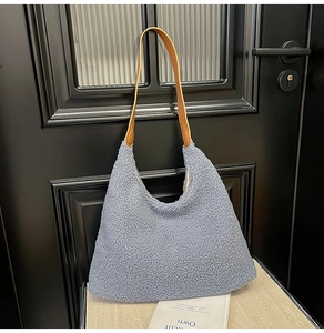 Close-up of blue plush tote bag with brown leather strap hanging on a door handle