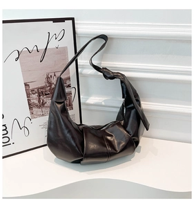 Detail shot of black pleated faux leather bag with decorative knot and smooth metal zipper