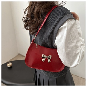 Detail of red faux leather shoulder bag featuring a silver bow accent and zipper closure