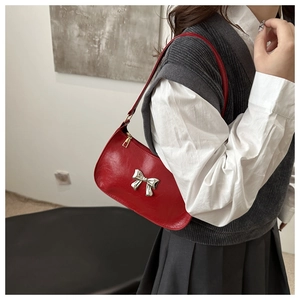 Detail view of a red hobo bag with silver bow buckle and shoulder strap on model