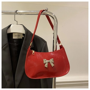 Detail of red patent leather underarm bag featuring a metallic silver bow ornament