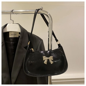 Detail of black glossy faux leather handbag with silver metallic butterfly accent