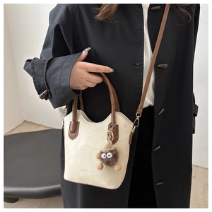 Detail of a beige bucket bag with brown handles and a cute plush monster charm