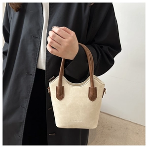 Detail of beige suede bucket bag with brown leather handles and embossed fashion logo