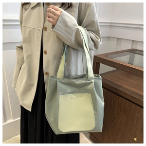 Sage green and yellow nylon tote bag with front pocket shown in a daily lifestyle setting