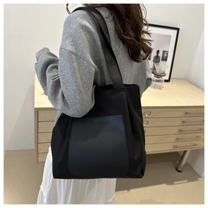 Detail of minimalist black nylon tote bag with leather pocket and shoulder strap