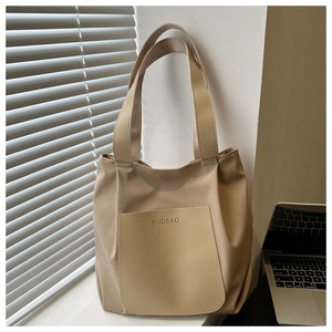 Detail of khaki tote bag with front pocket and logo on a desk with laptop