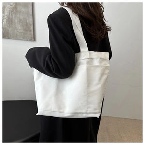 Detail of white canvas tote bag with side pockets and wide strap on model
