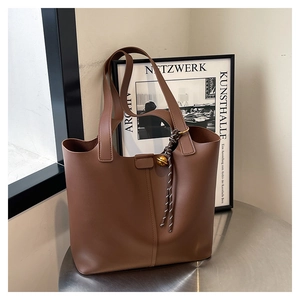 Detail of dark brown leather tote bag with braided charm on a metallic table
