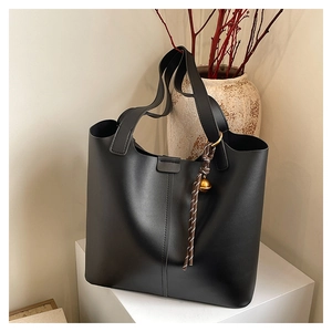 Detail of a large black matte tote bag featuring vertical stitching and a braided bell charm