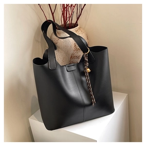 Detail of black tote bag featuring gold hardware rings and woven rope pendant on a white stand