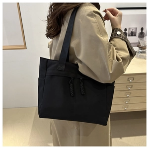 Détail d'un grand sac cabas noir en toile porté sur une gabardine kaki de style urbain